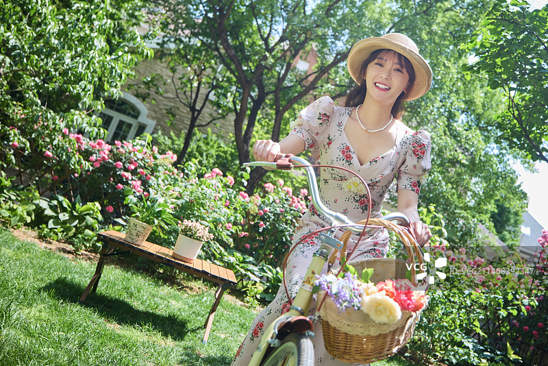 青年美女在开满鲜花的院子里骑自行车图片素材