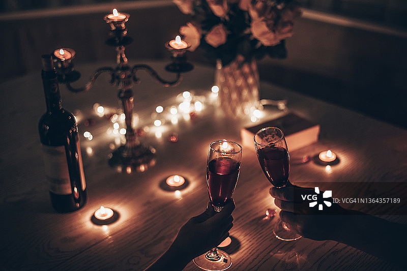 手握酒杯的男人和女人在家里的餐桌上度過浪漫的燭光晚餐。手握酒杯的男人和女人。情人節或夜晚燭光約會的概念。圖片素材