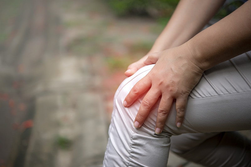一位老婦人在公園里飽受膝蓋疼痛之苦。抱著膝蓋，用手按摩。圖片素材
