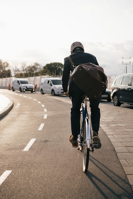 在陽光明媚的日子里，商人在城市街道上騎自行車的后視圖圖片素材