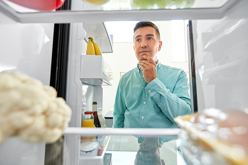 飲食概念-微笑的中年男人男人在廚房的冰箱里尋找食物。在廚房冰箱里找食物的人圖片素材
