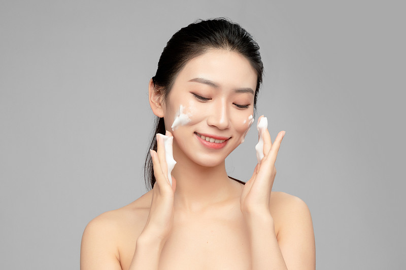 灰色背景里正在使用洗面奶的亞洲美女面部特寫，化妝護膚整容圖片素材