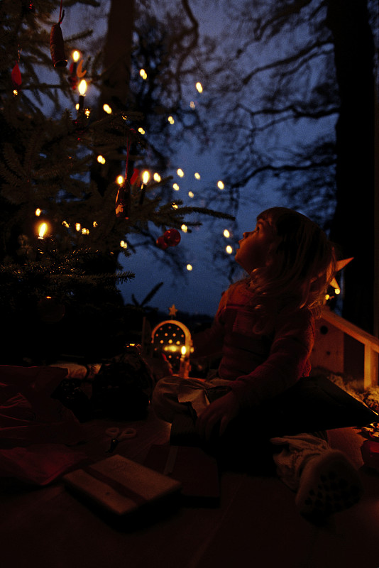 小女孩坐在圣誕樹前圖片素材