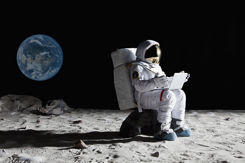 月球上的宇航员坐在一块岩石上用笔记本电脑图片下载