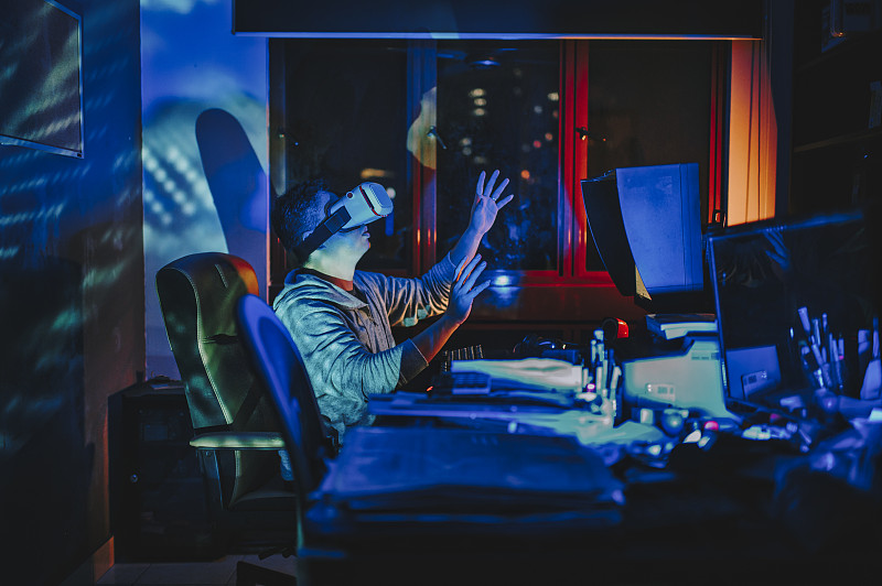 一名亞洲華人男性戴上VR眼鏡，在他的家庭辦公室自修室里，在他的臺式電腦前體驗3D虛擬游戲體驗圖片素材