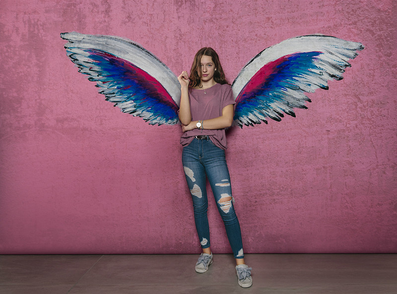 少女站在粉紅色墻上天使翅膀涂鴉圖片素材