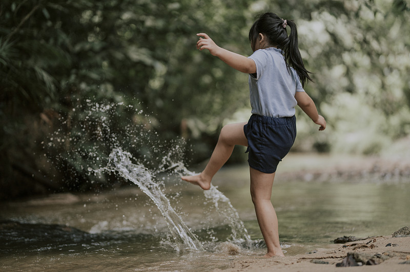 一個亞洲的中國小女孩在河里玩在周末娛樂追求踢水濺的樂趣圖片素材