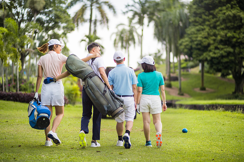 一個亞洲華人家庭微笑著在高爾夫球場享受他們的周末活動。他們正走向高爾夫球車。圖片素材