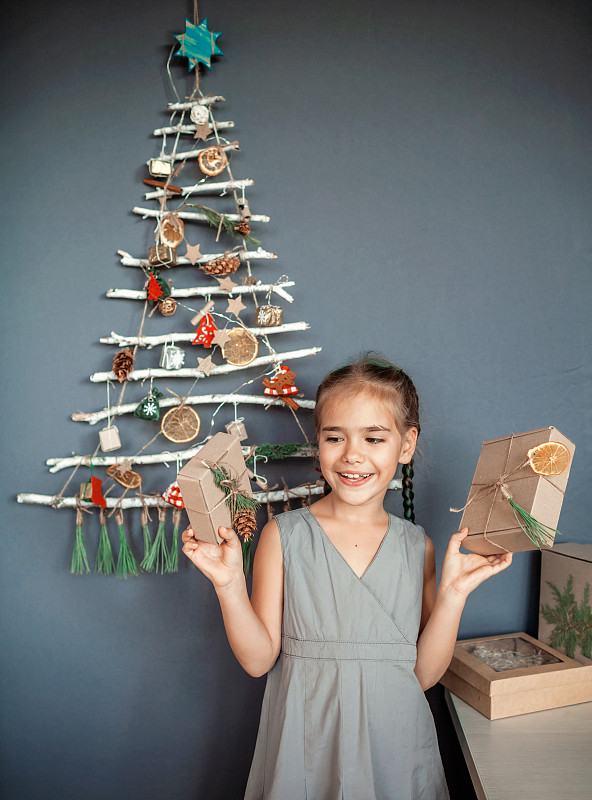 微笑的女孩拿著禮物對著掛在墻上的圣誕樹圖片素材