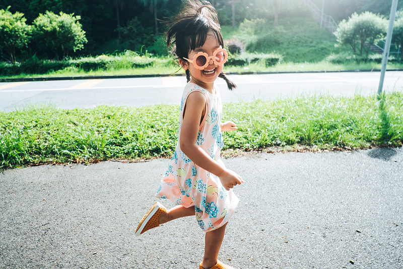 快樂的亞洲小女孩戴著花形太陽鏡在公園里跑步。享受大自然和夏日戶外。她對著鏡頭微笑。童年的生活方式，無憂無慮的自由理念圖片下載