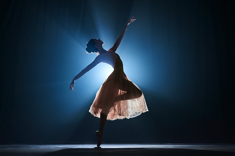 迷人的，艺术的，有才华的年轻女孩，芭蕾舞演员跳着古典舞蹈，在深蓝色的聚光灯下表演图片下载