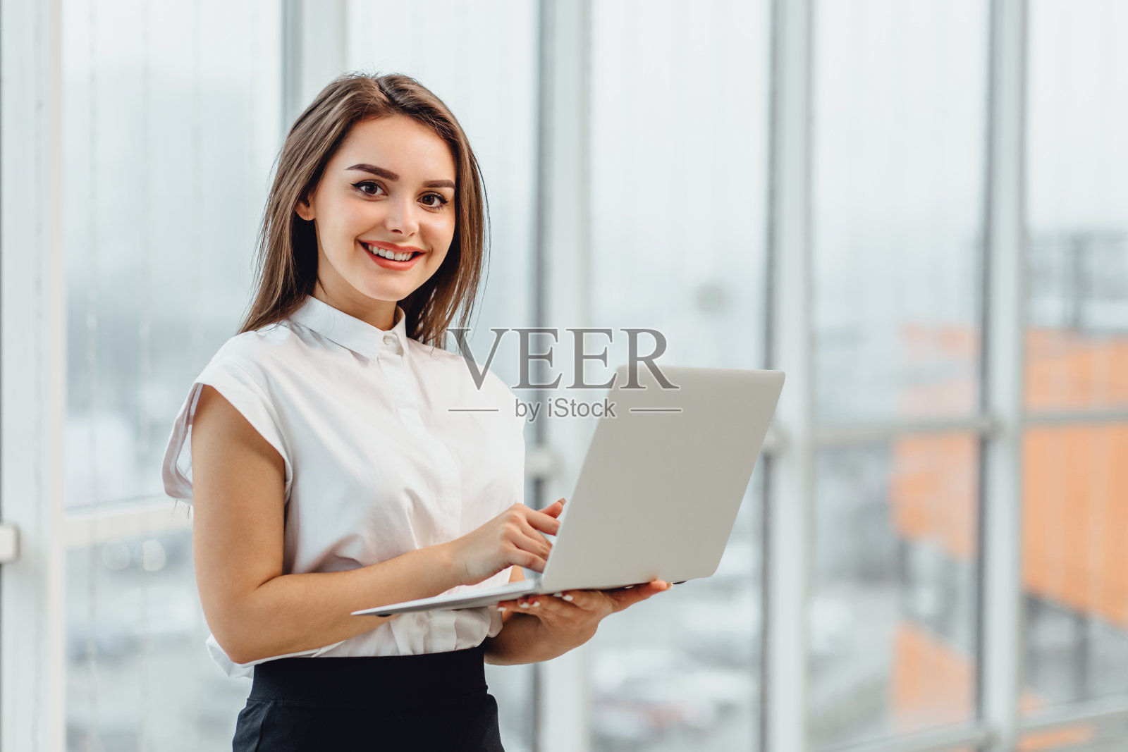 快樂的商務女性站在辦公室，拿著筆記本電腦。照片攝影圖片