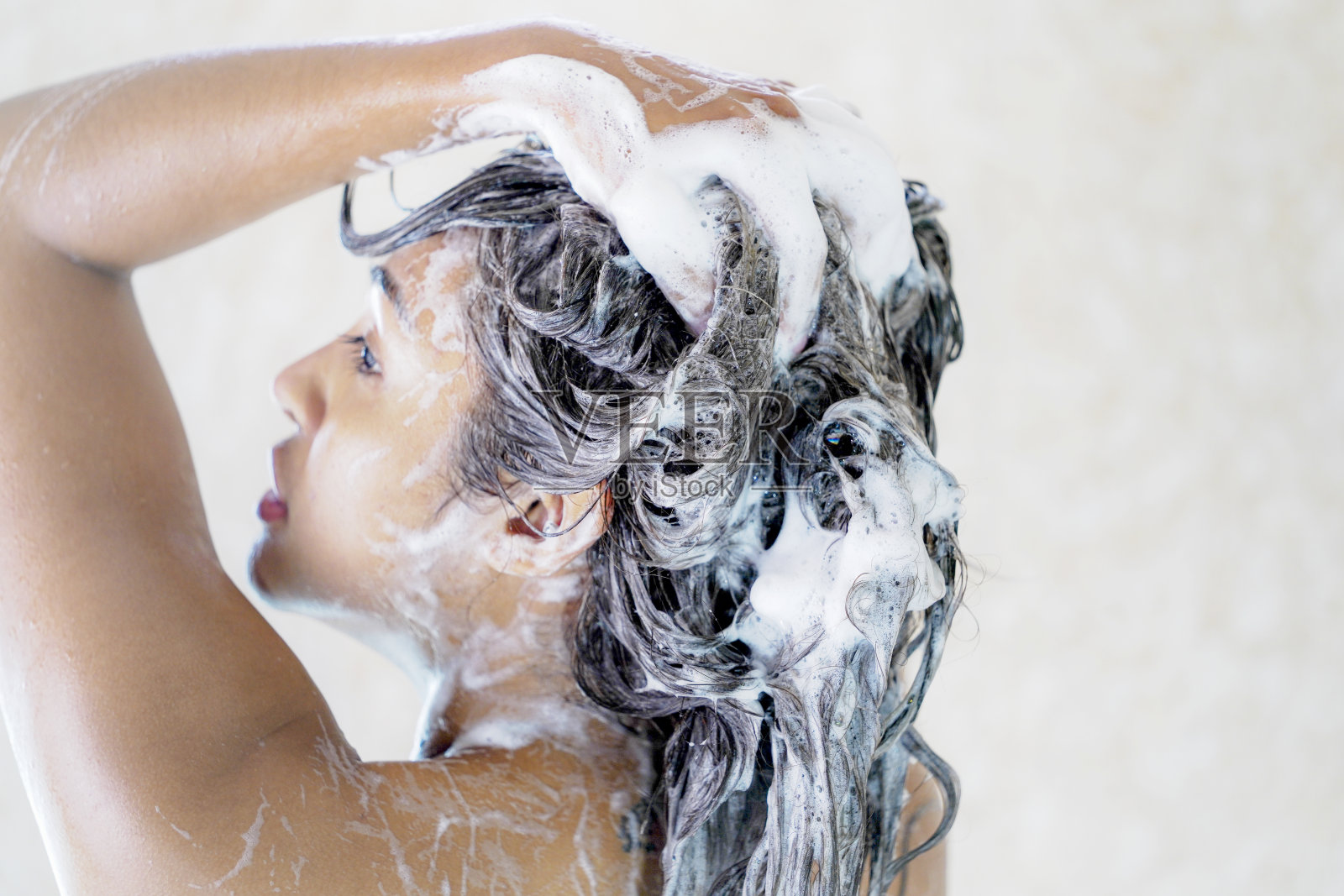 年轻女子在淋浴时用泡沫去屑洗发水洗头。照片摄影图片
