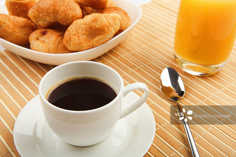 早餐咖啡和牛角面包放在桌子上，背景很亮。图片素材