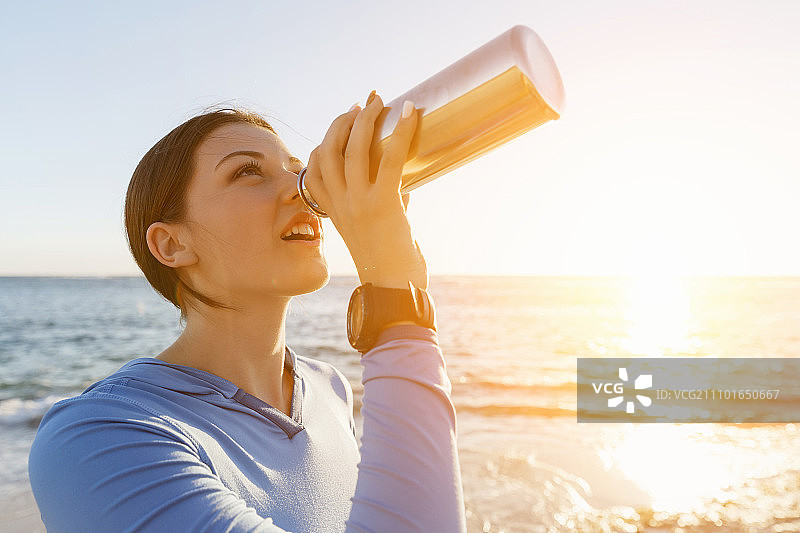 在海滩上喝水的女人。年轻女子在海滩锻炼后喝水图片素材