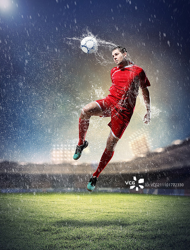 足球运动员击球。穿着红衬衫的足球运动员冒雨在体育场里击球图片素材