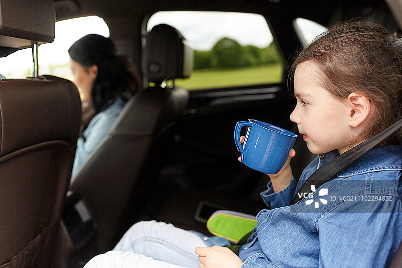 家庭，交通，公路旅行和人的概念-小女孩开车与母亲和喝从杯子图片素材