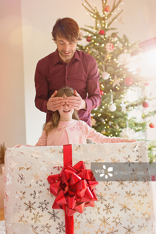 父亲捂着女儿的眼睛，拿着大大的圣诞礼物图片素材