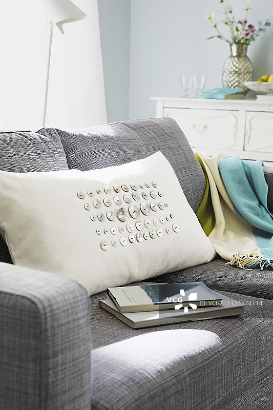 奶油色枕头和珍珠纽扣缝在灰色沙发和书周围图片素材