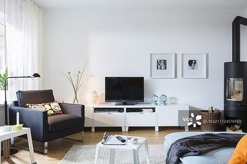 客厅里的一台电视机前有一张黑色的扶手椅，上面有一个斯堪的纳维亚式的木火炉图片素材