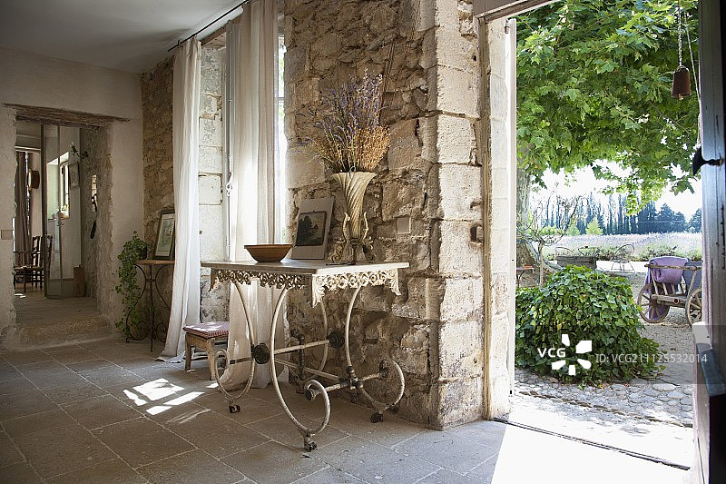 精致、古老的金属桌子靠在质朴的石墙上，透过敞开的门可以看到花园图片素材