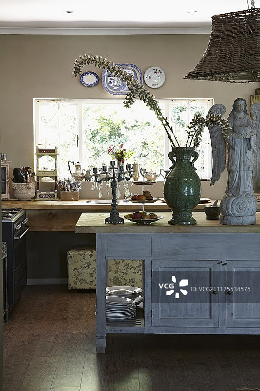 在开放式厨房的古董木餐具柜上，天使雕像旁边的绿色花瓶上盛开的树枝图片素材