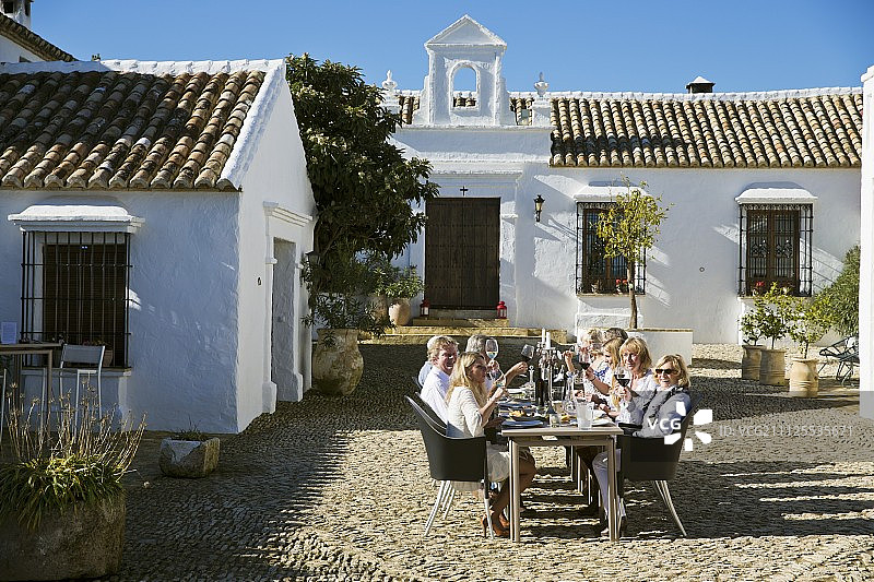 一群成年人坐在地中海乡村住宅的鹅卵石庭院里的长桌旁图片素材