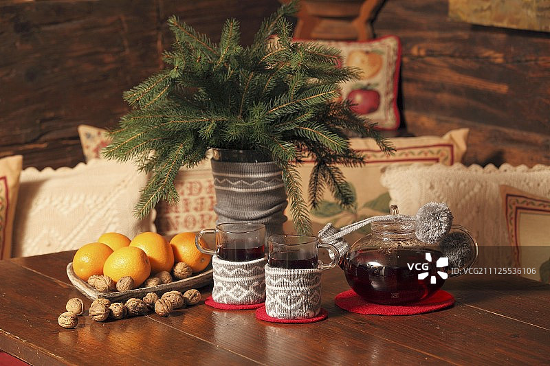 杯茶和冷杉树枝插在花瓶上编织盖旁边的茶壶和节日的水果和坚果在木屋的木桌上图片素材
