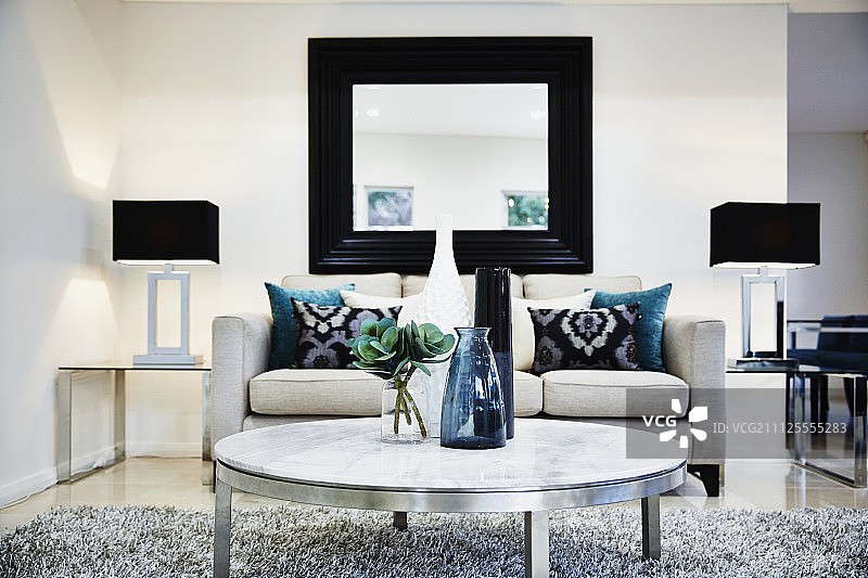现代客厅，沙发，镜子在墙上，金属桌子，地毯和灯在玻璃边桌图片素材