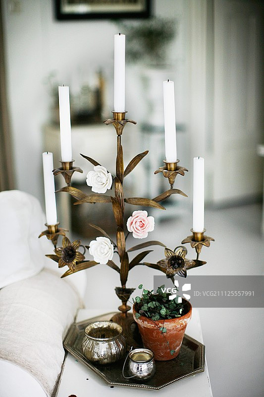 白色蜡烛在黄铜，花卉烛台与彩色玫瑰装饰托盘在盆栽植物和银罐图片素材