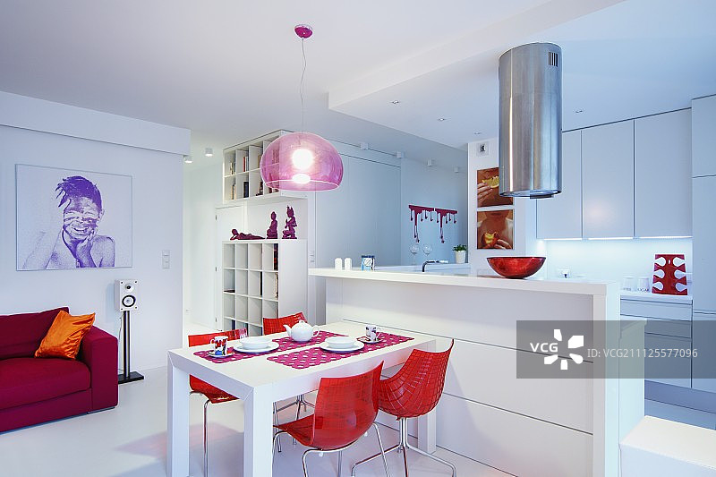 在开放式室内，红色贝壳椅围绕着餐桌，靠着白色厨房柜台图片素材