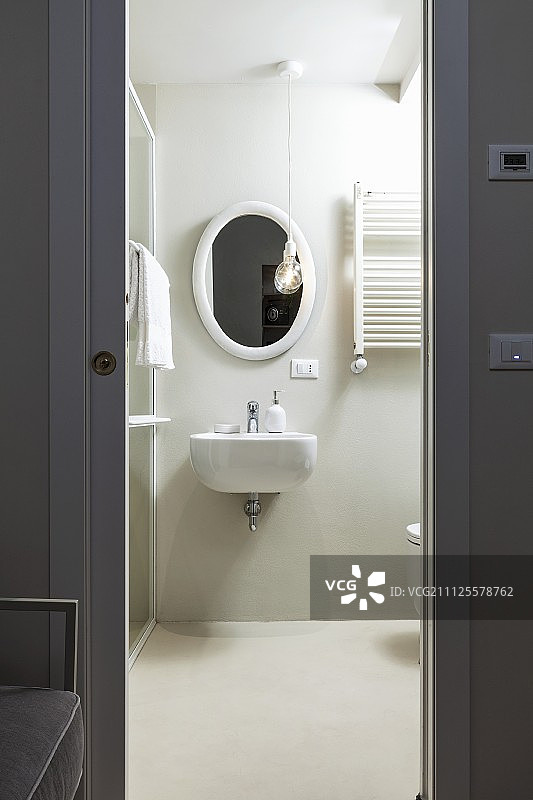 透过灰色的推拉门，可以看到带有椭圆形镜子和水槽的白色浴室图片素材