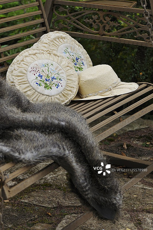 太阳帽，两个老式的绣花靠垫和毛皮毯子上的古董花园秋千图片素材