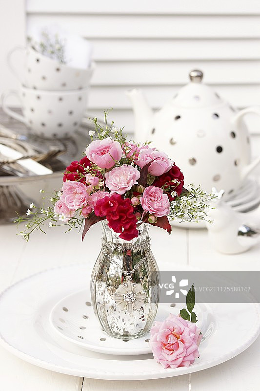 一束带有鸡冠和吉普赛花的银色玻璃花瓶放在圆点茶具前图片素材