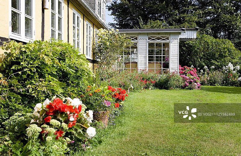 夏季花园，有整洁的草坪和开花植物，屋外有温室图片素材