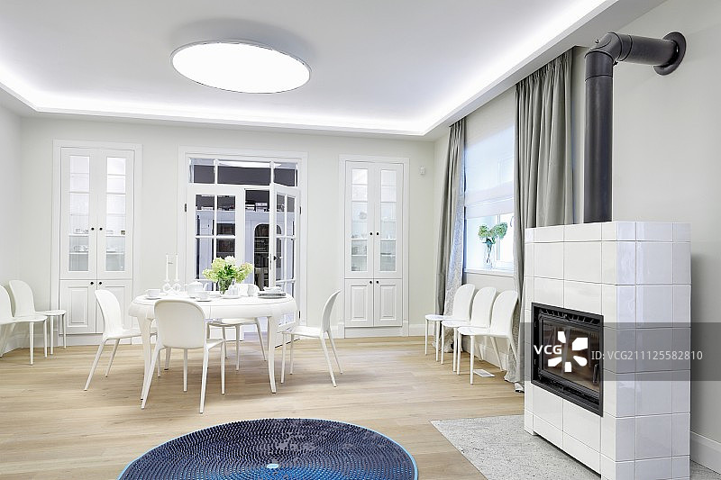 白色室内靠墙放置餐具和额外的椅子;蓝色的地毯在前面的瓷砖燃烧木材的火炉图片素材