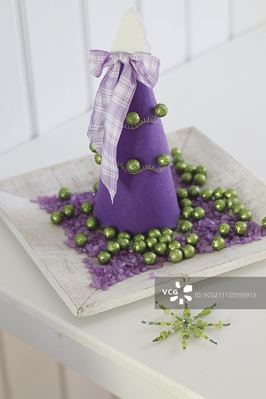 紫色的毛毡圣诞树在盘子上，紫色的砂砾和绿色的小装饰品图片素材
