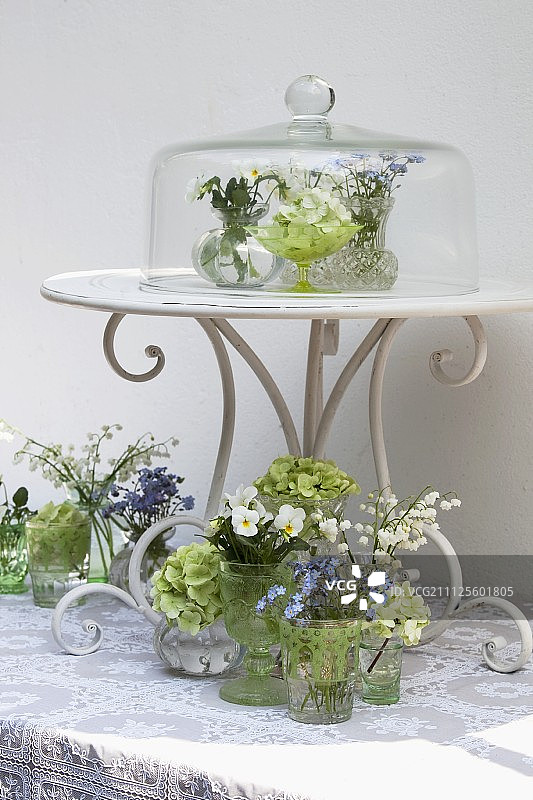 在桌子上和玻璃盖下摆放装着春天鲜花的小花瓶图片素材