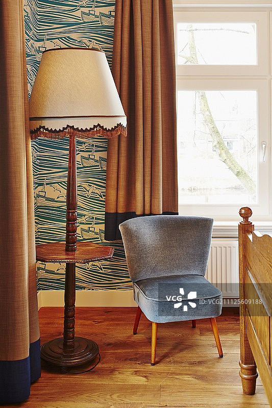 卧室里的舒适椅子配有石板灰色天鹅绒罩，旁边是50年代风格的标准灯，木制底座和集成书架图片素材