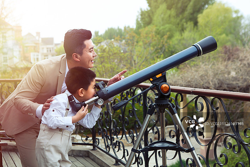 父亲和儿子在阳台使用天文望远镜图片素材