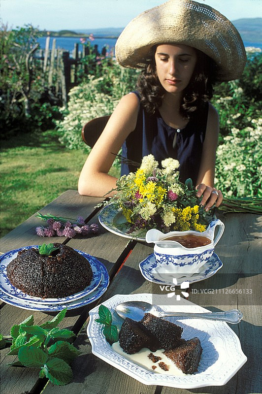 花园桌上放着苏格兰布丁，后面有个年轻女人图片素材