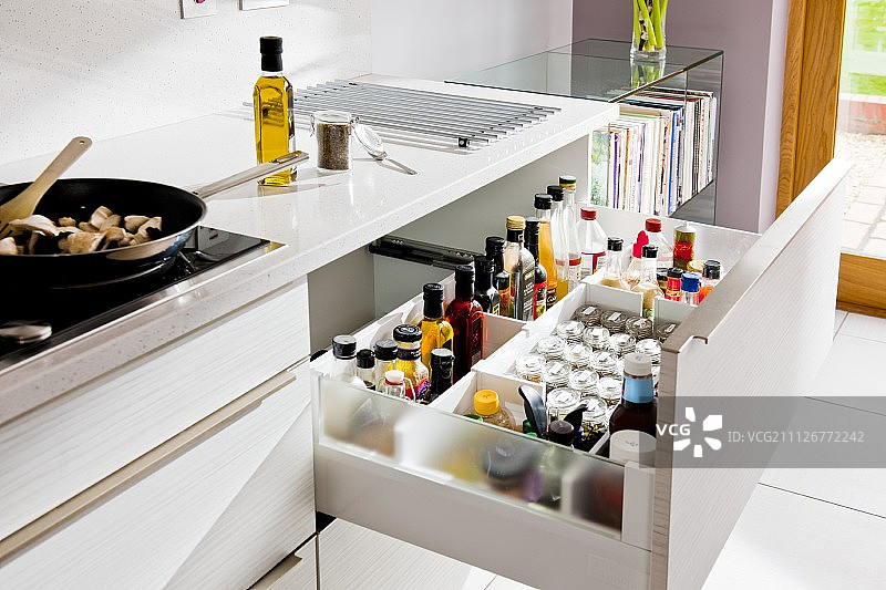白色的厨房柜台上有一个打开的抽屉，里面放着香料和瓶子图片素材