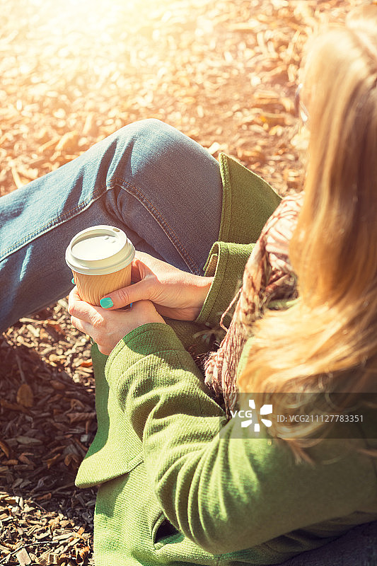 秋天的概念，匿名女子享受外卖咖啡杯在阳光明媚的寒冷秋天的一天图片素材