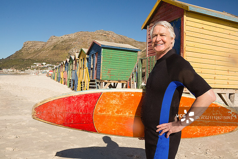 一位带着冲浪板站在海滩小屋前的老人的肖像图片素材