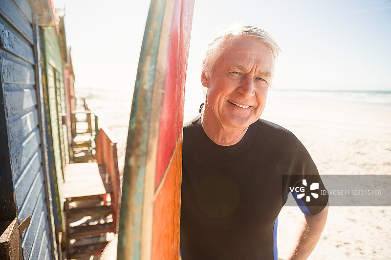 微笑的老人站在海滩冲浪板旁的肖像图片素材