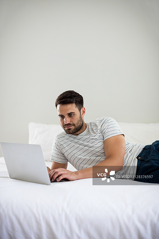 一个男人在卧室的床上用笔记本电脑图片素材