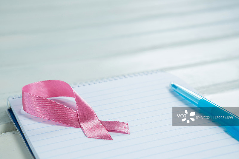 高角度的粉红色乳腺癌意识丝带和螺旋记事本与钢笔在木桌上图片素材