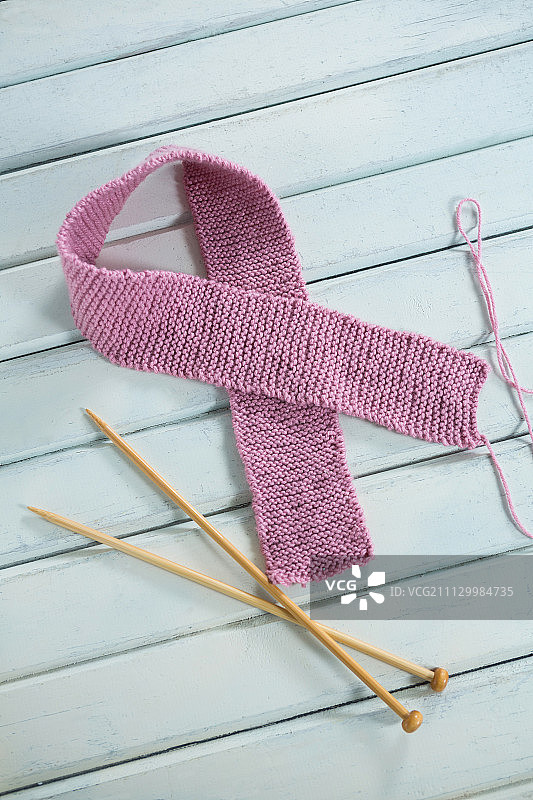 高角度的粉红色羊毛乳腺癌意识丝带钩针在白色木制桌子上图片素材