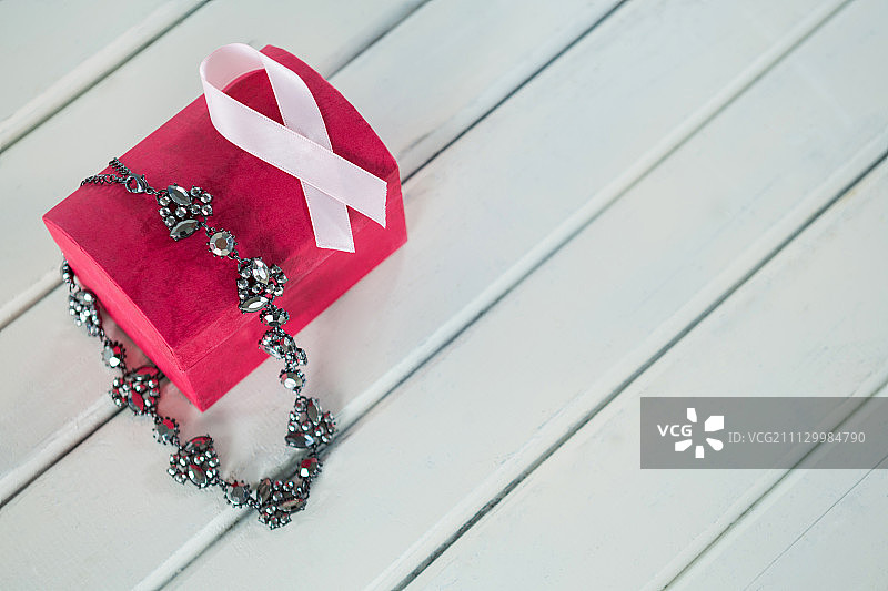 高角度的珠宝，红色的盒子和粉红色的乳腺癌意识丝带放在木桌上图片素材