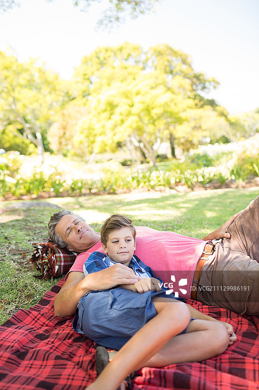 在一个阳光明媚的日子里，父亲和儿子躺在野餐毯上图片素材